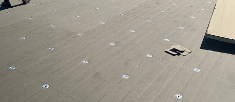 Roof boards secured with rows of plates and fasteners during installation.